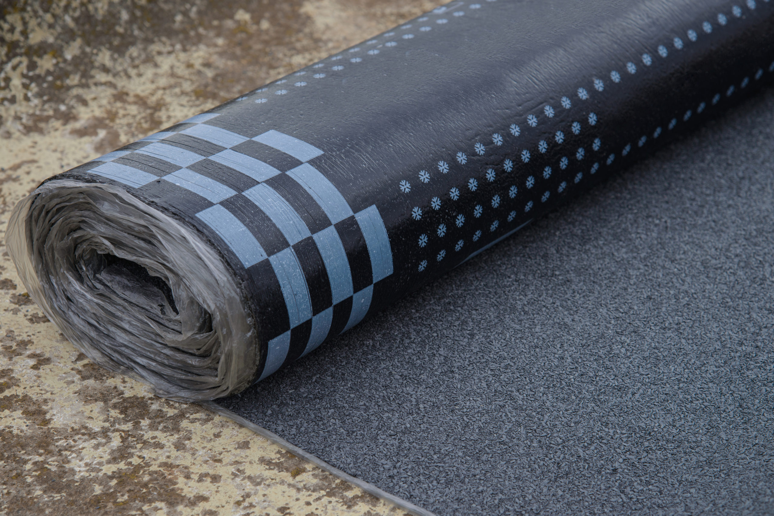 A bitumen waterproofing membrane rests partially unrolled on the ground.